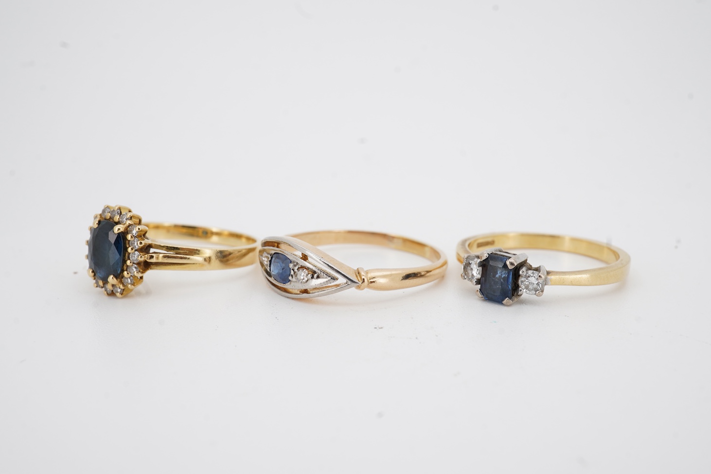A modern 18ct gold, single stone sapphire and two stone diamond set ring, size O, an 18k, sapphire and diamond set oval cluster ring, size M/N and an 18ct, single stone sapphire and two stone diamond chip set navette sha